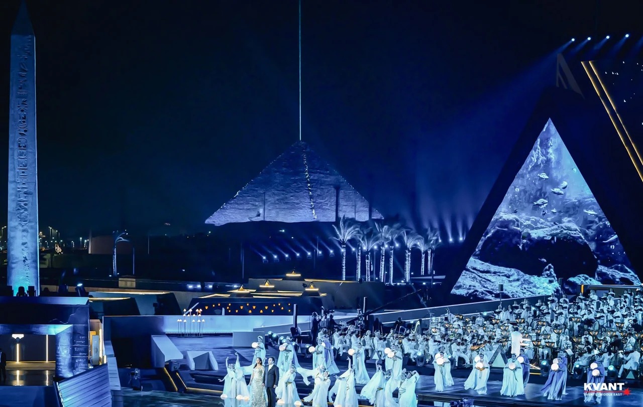 Osvetlená scéna s účinkujúcimi pred pyramídami